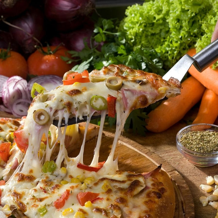 Slice of veggie pizza being lifted surrounded by fresh vegetables.