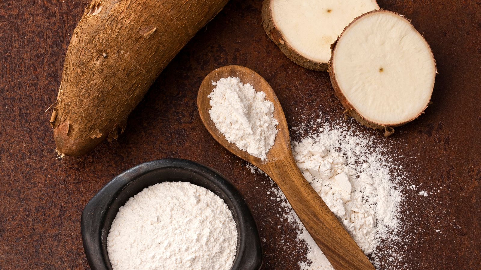 Tapioca flour on spoon with sliced and whole cassava root.