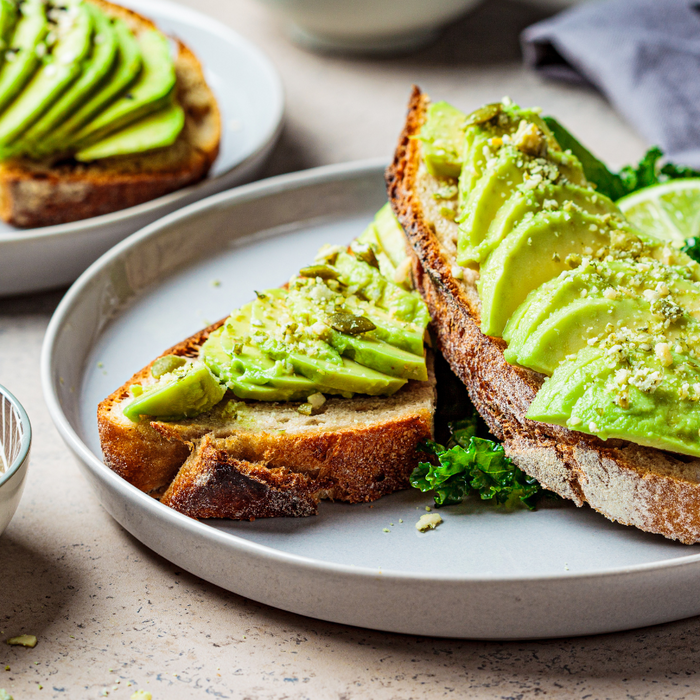 Avocado toast with sliced avocado and kale served on sourdough bread.
