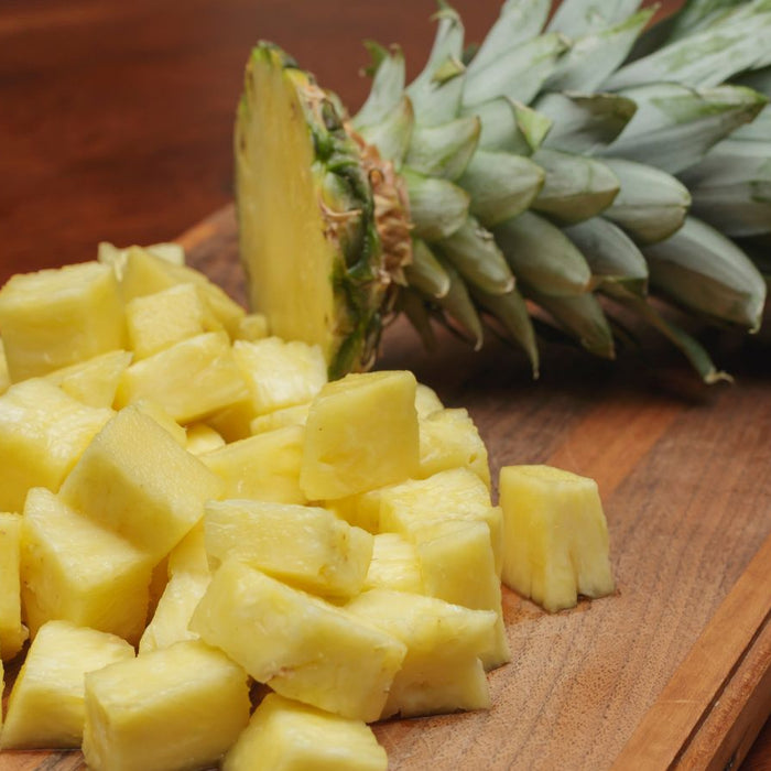 Cubed pineapple pieces and fruit on cutting board.