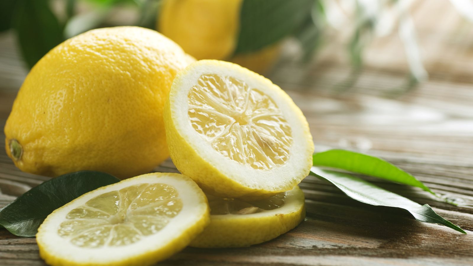 Whole and sliced lemons on wooden table with fresh green leaves