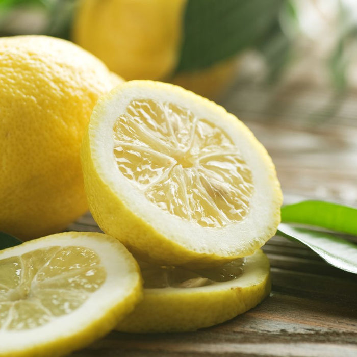 Whole and sliced lemons on wooden table with fresh green leaves