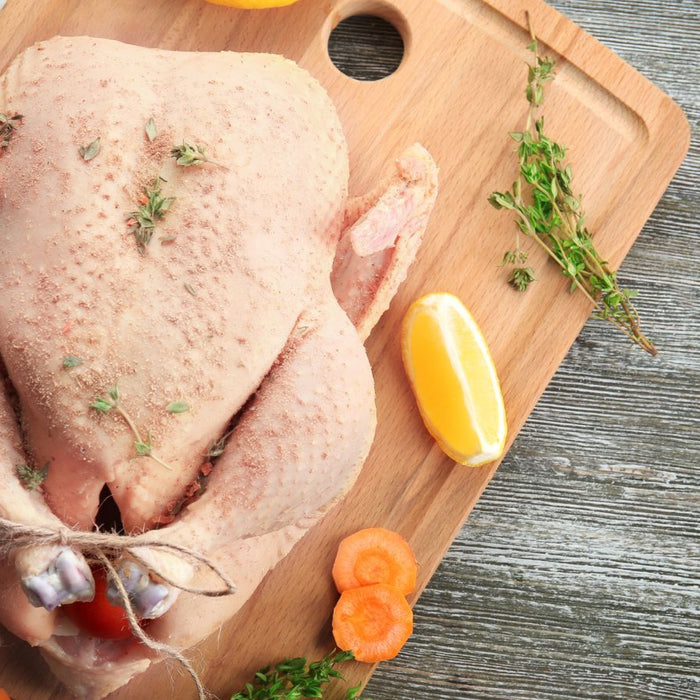 Uncooked whole turkey seasoned with herbs on a wooden cutting board