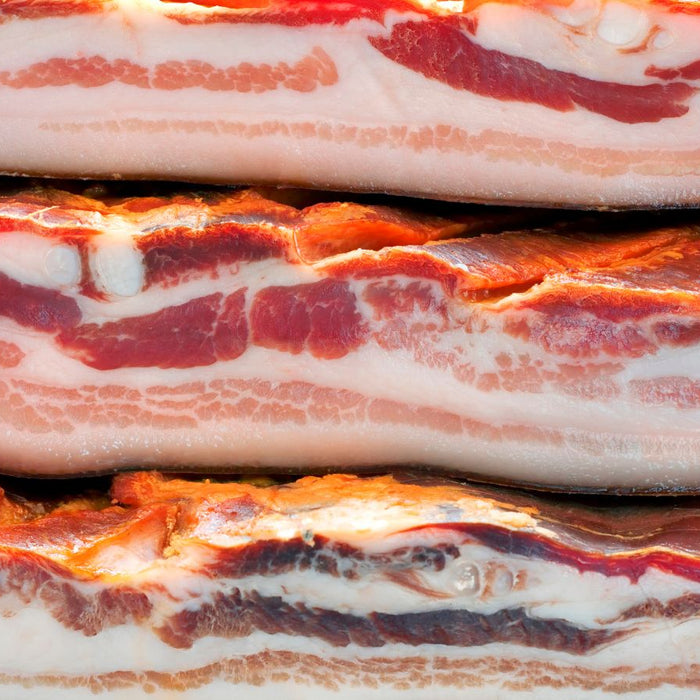 Thick slabs of smoked bacon stacked on a wooden cutting board.