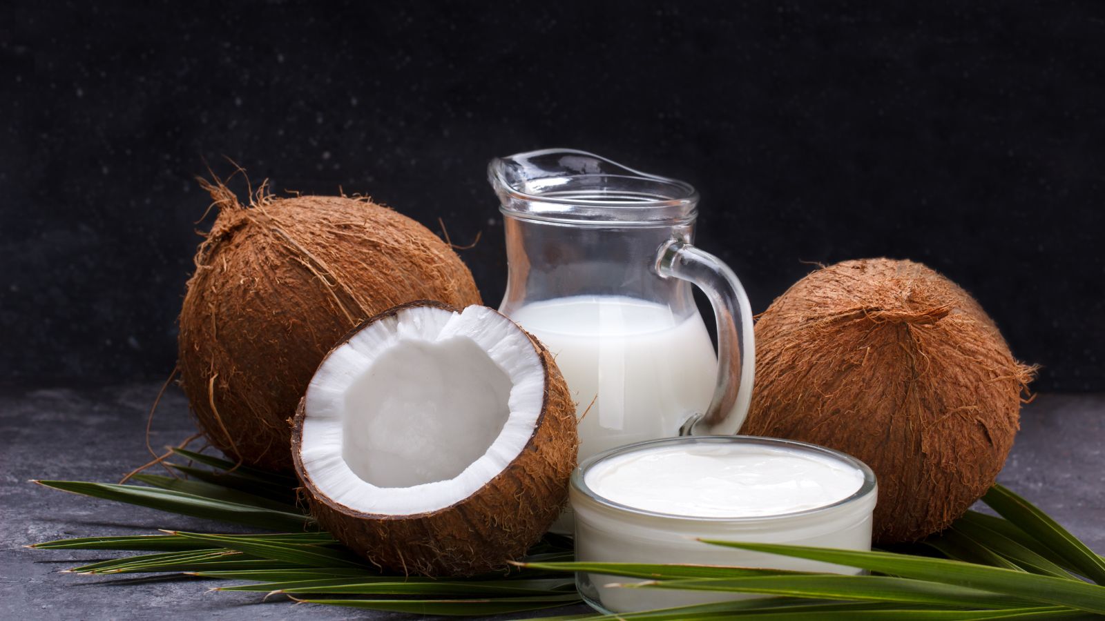 Whole coconuts with glass of coconut milk and cream on table