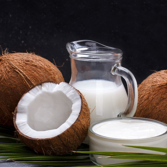 Whole coconuts with glass of coconut milk and cream on table