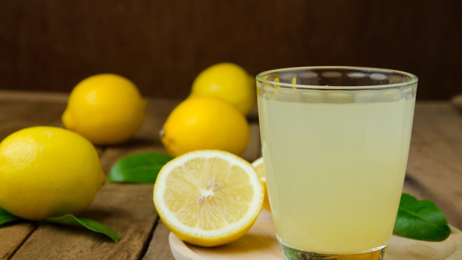 Glass of fresh lemon juice with lemons on rustic wooden table