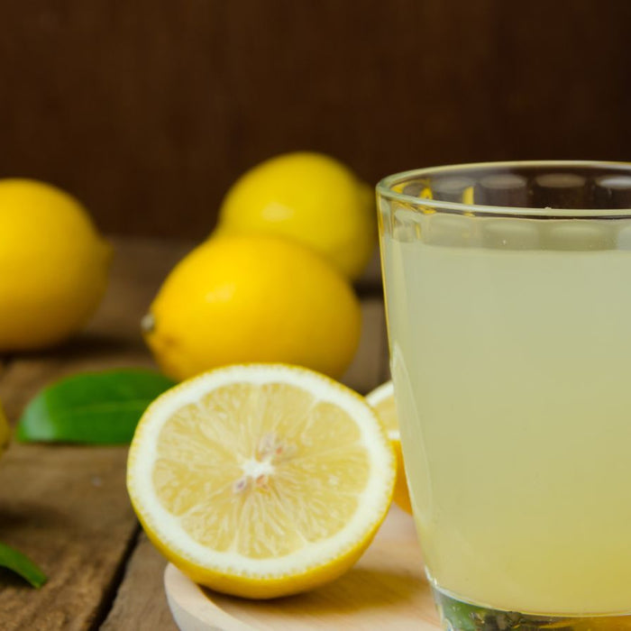 Glass of fresh lemon juice with lemons on rustic wooden table