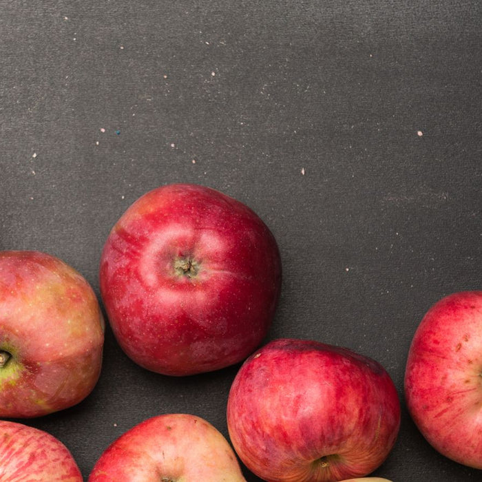 Group of red and green apples on black textured background.