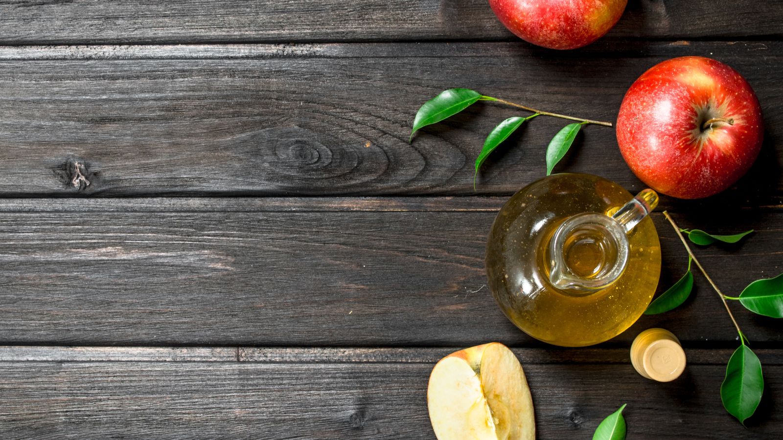 Top view of apples with glass jug of apple cider vinegar on wood table