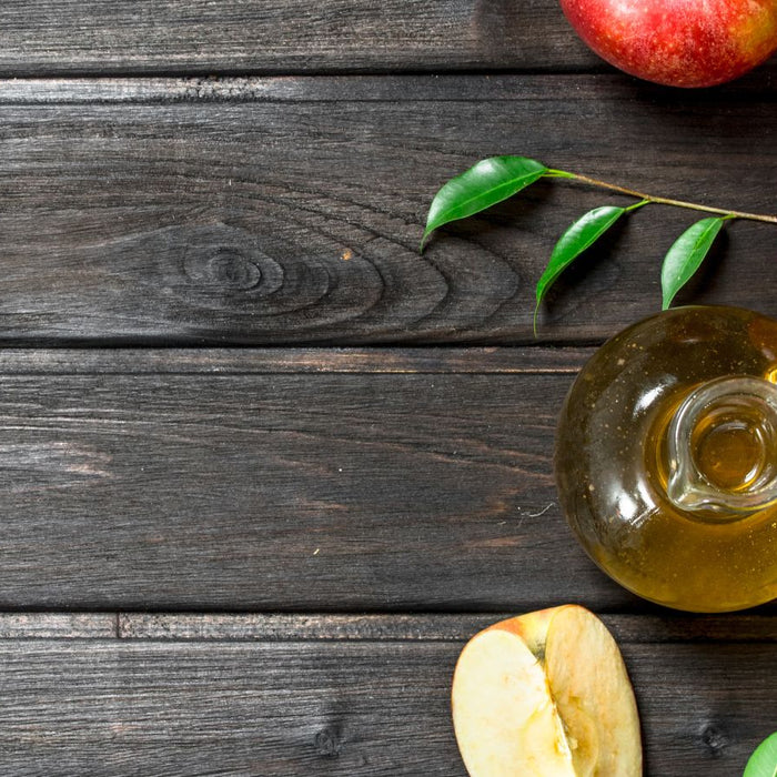 Top view of apples with glass jug of apple cider vinegar on wood table