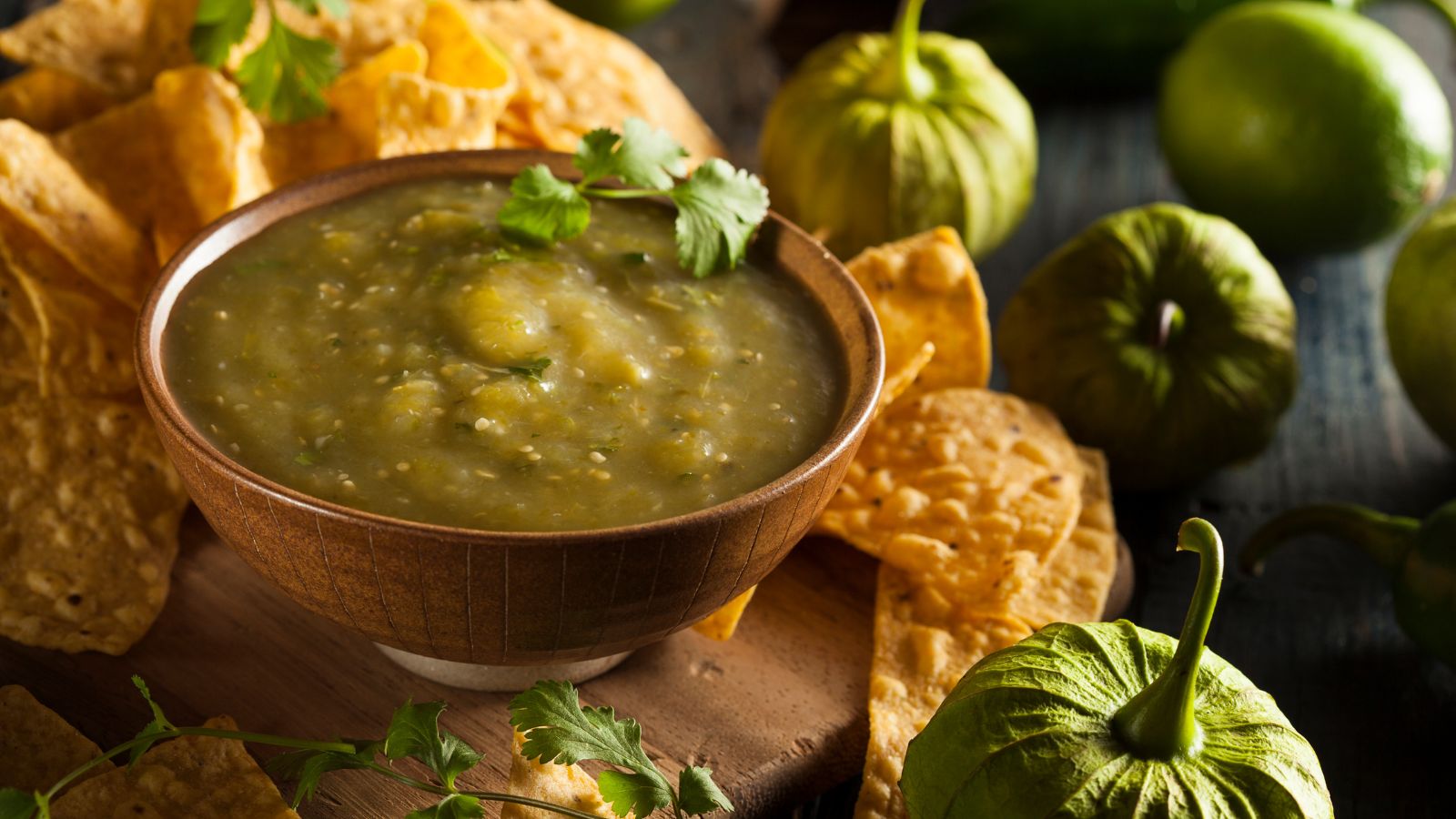 Green tomatillo salsa in a bowl with tortilla chips and garnish.