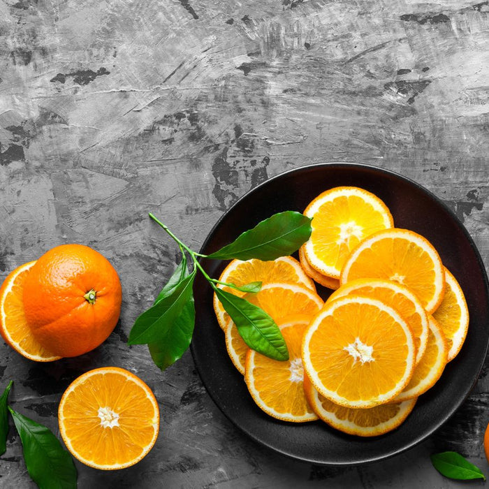 Black plate of orange slices with whole oranges and green leaves.