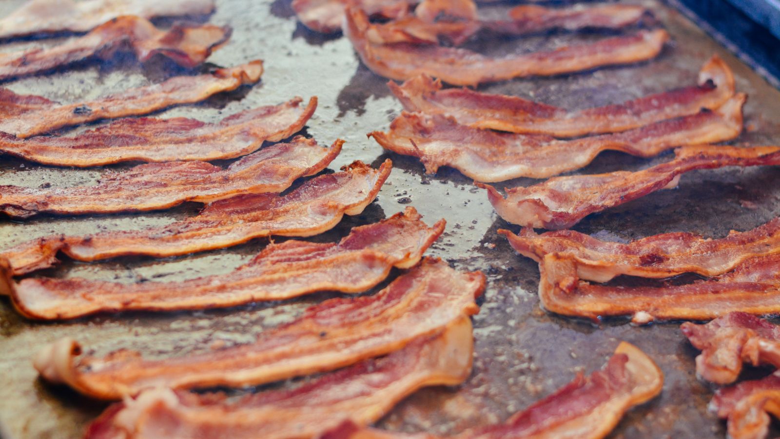 Strips of crispy bacon cooking on a large griddle surface.