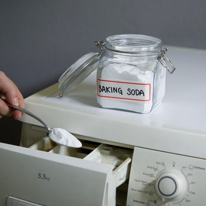 Hand scooping baking soda into washing machine detergent drawer.