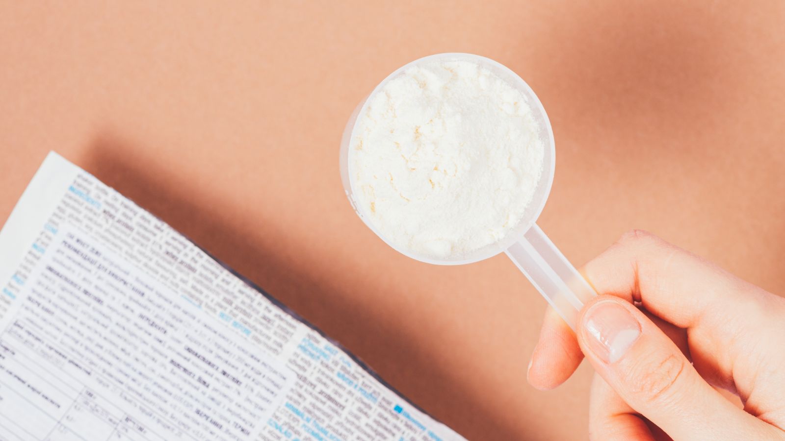 Hand holding scoop of white protein powder above product label