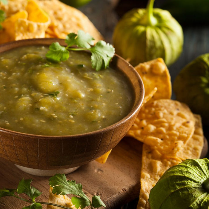 Green tomatillo salsa in a bowl with tortilla chips and garnish.