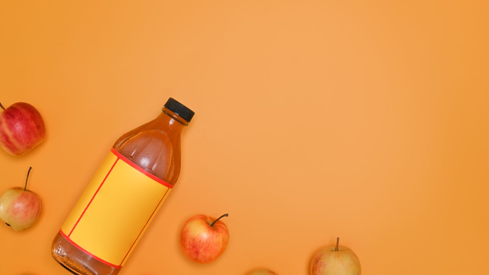 Bottle of apple cider vinegar with fresh apples on orange background.