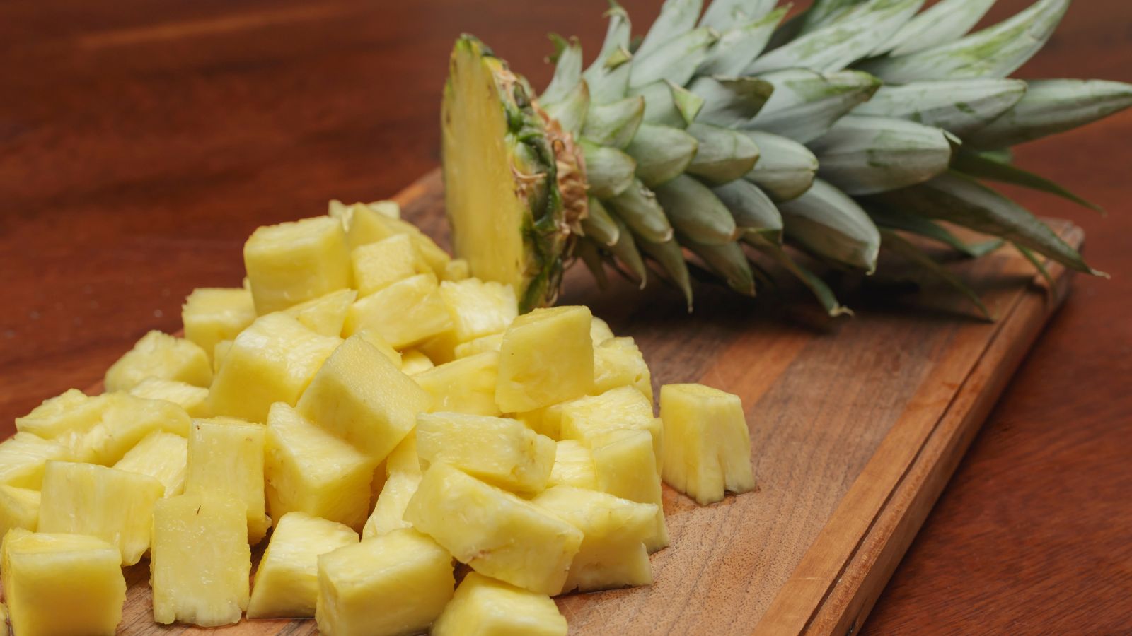 Cubed pineapple pieces and fruit on cutting board.