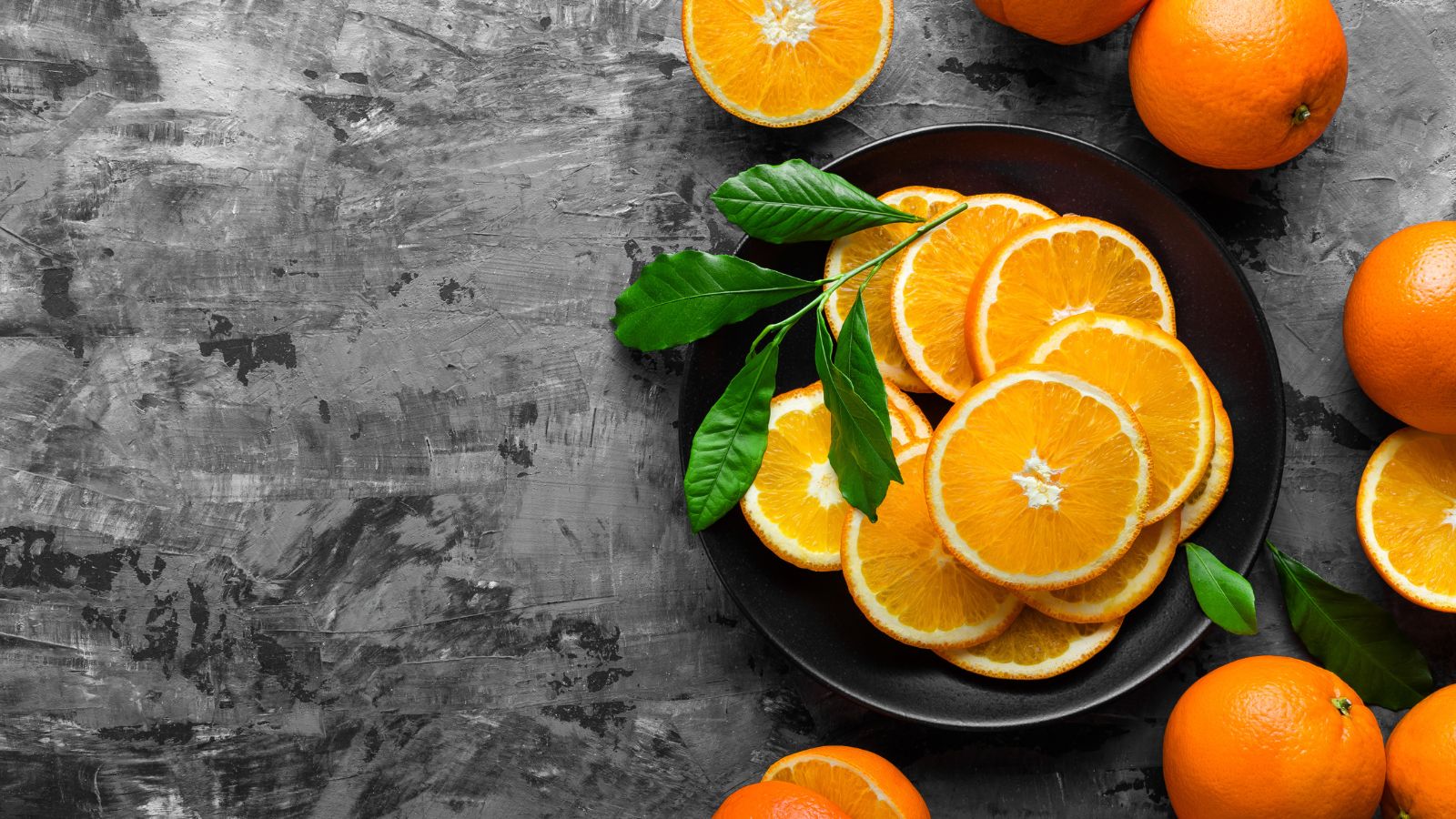 Fresh orange slices on black plate with whole oranges.