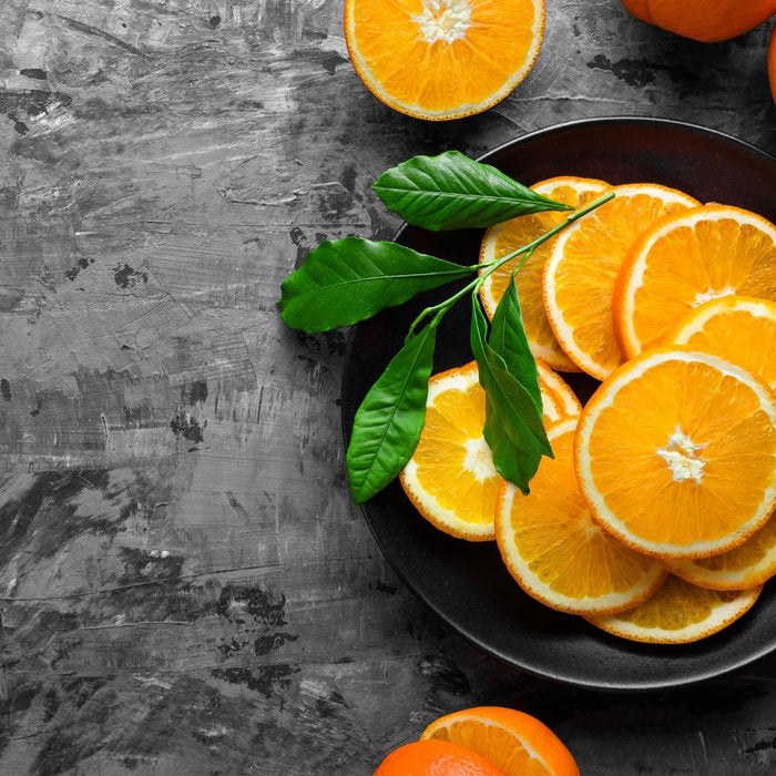Fresh orange slices on black plate with whole oranges.