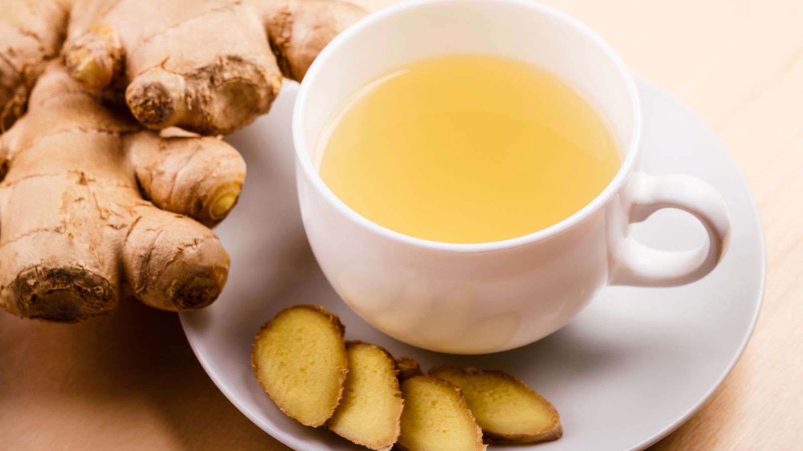 Cup of ginger tea with fresh and sliced ginger on saucer.