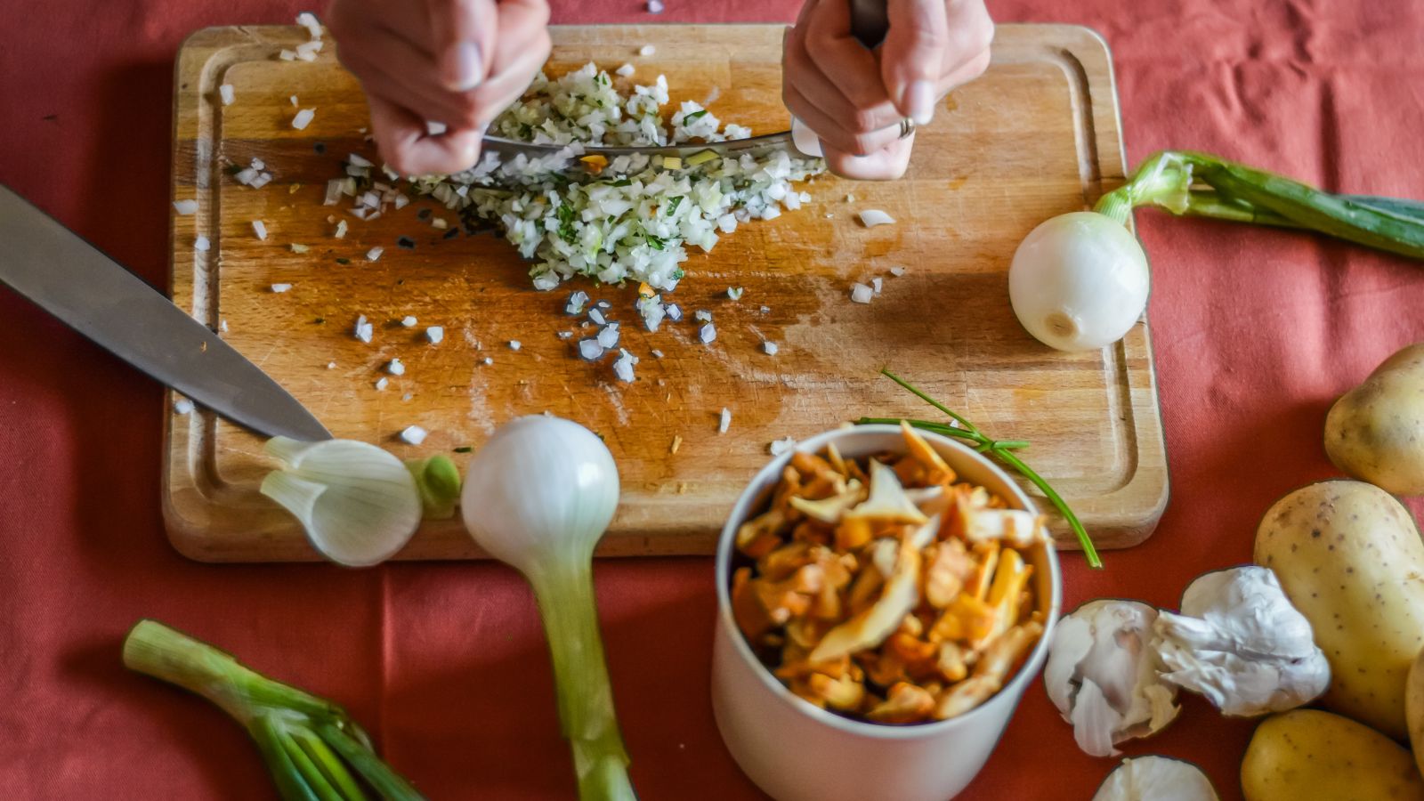 Chopping onions and herbs on cutting board with fresh vegetables.