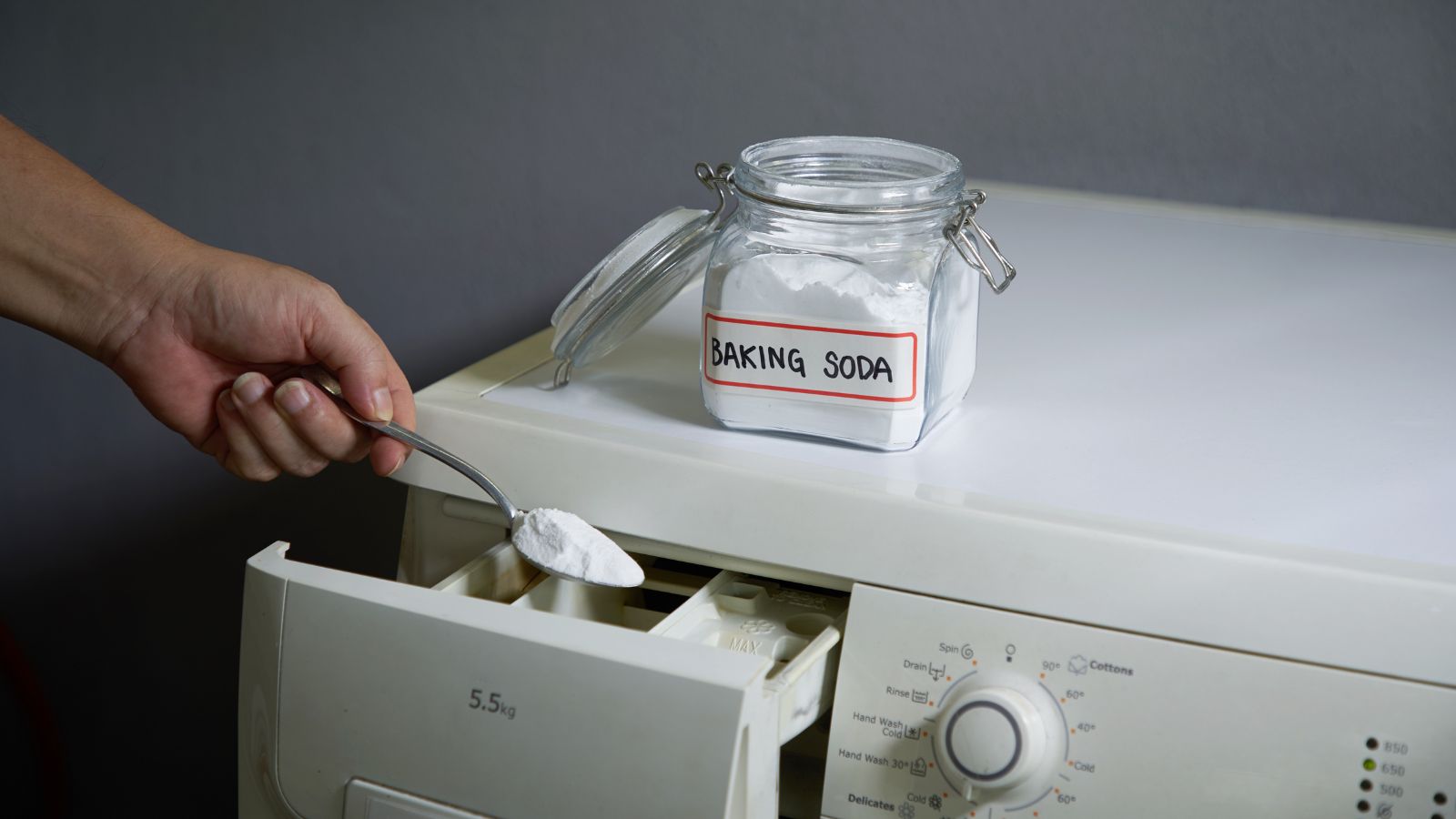 Hand scooping baking soda into washing machine detergent drawer.