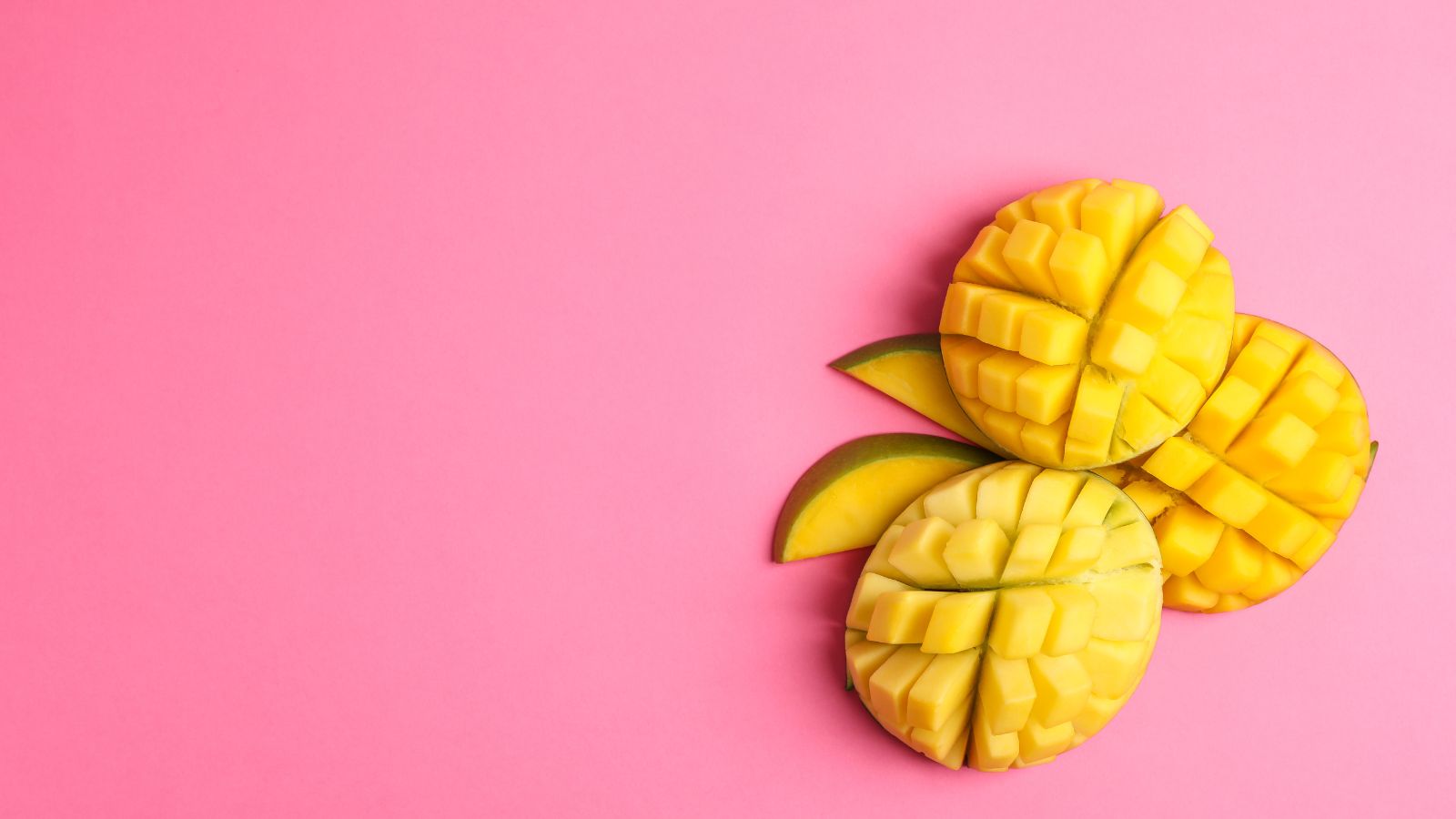 Three grid-cut mango halves arranged on pink background.