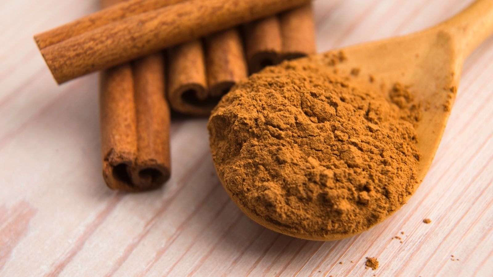 Ground cinnamon on wooden spoon with cinnamon sticks nearby.