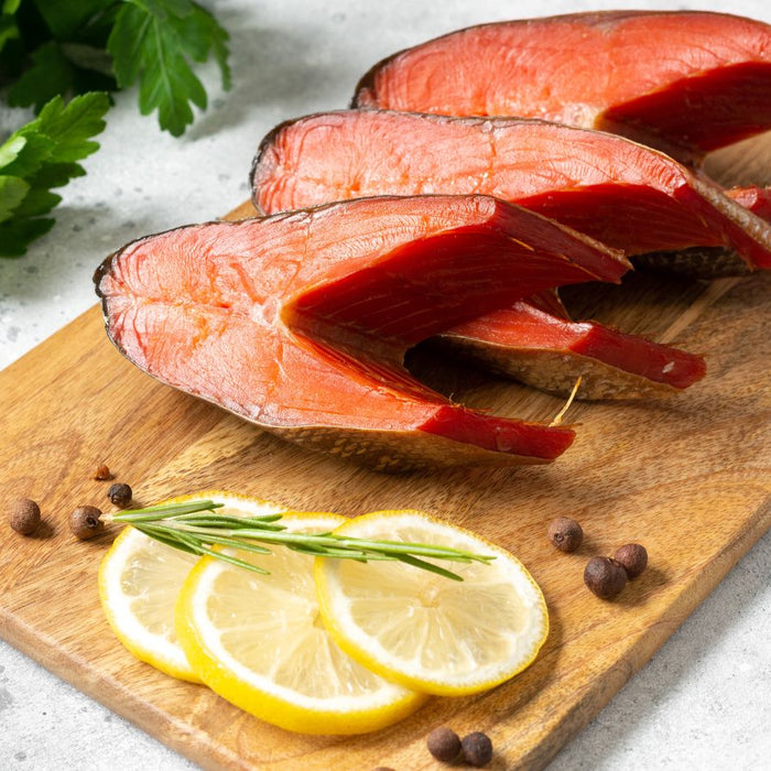 Sliced smoked salmon steaks on wooden board with lemon and herbs.