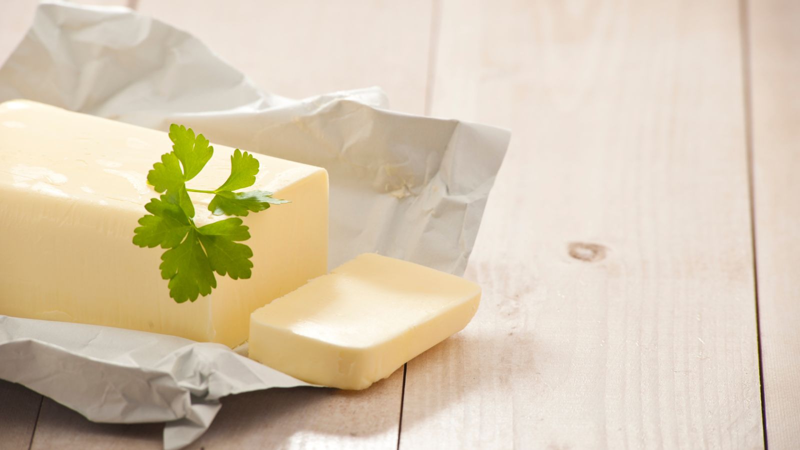 Butter block on parchment with parsley garnish on wooden surface.