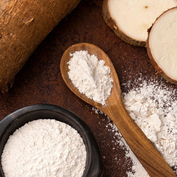 Tapioca flour on spoon with sliced and whole cassava root.