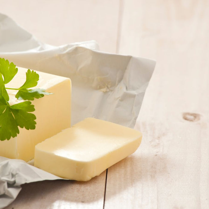 Butter block on parchment with parsley garnish on wooden surface.