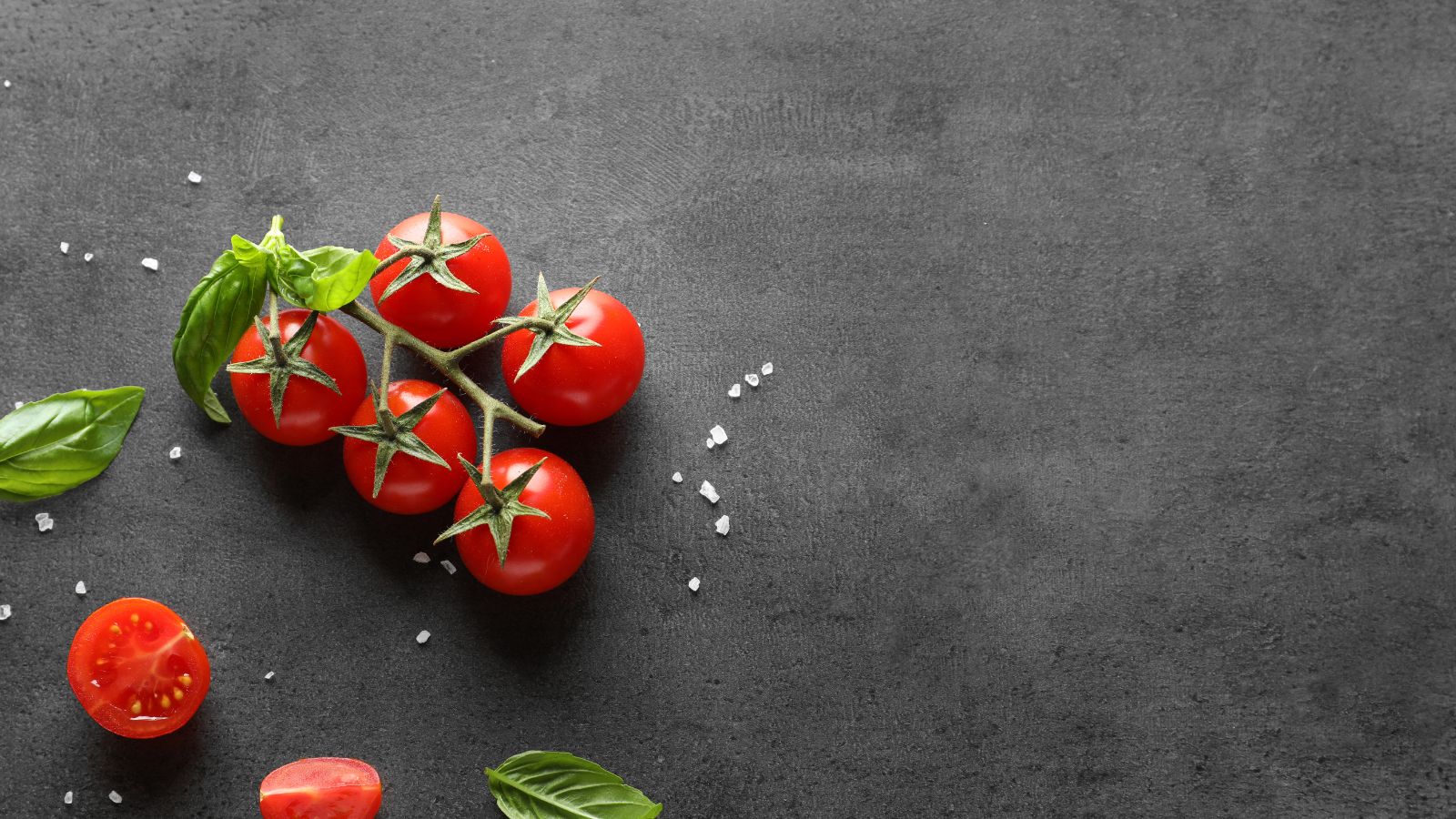Cherry tomatoes with basil and salt on black stone table background