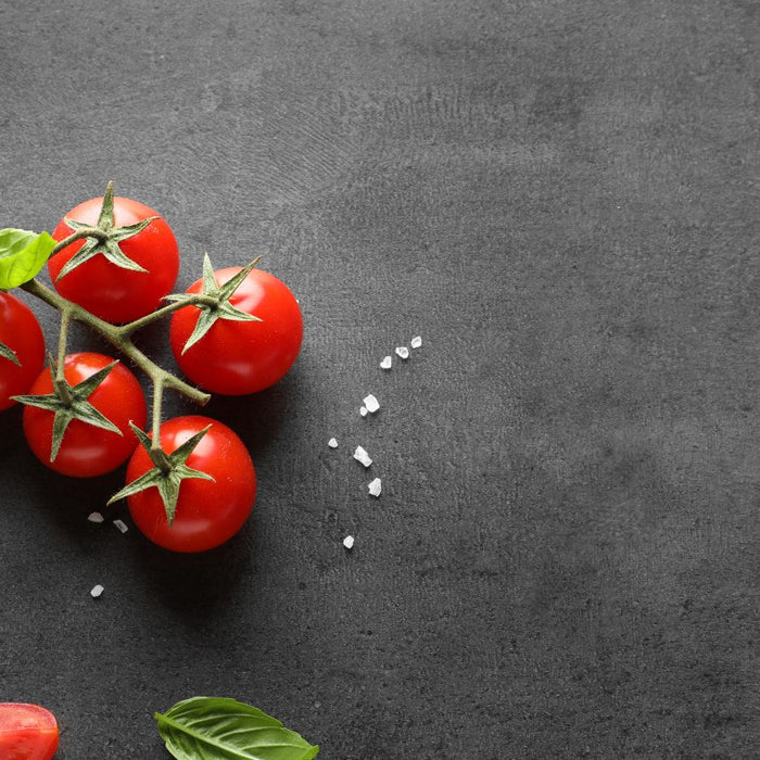Cherry tomatoes with basil and salt on black stone table background