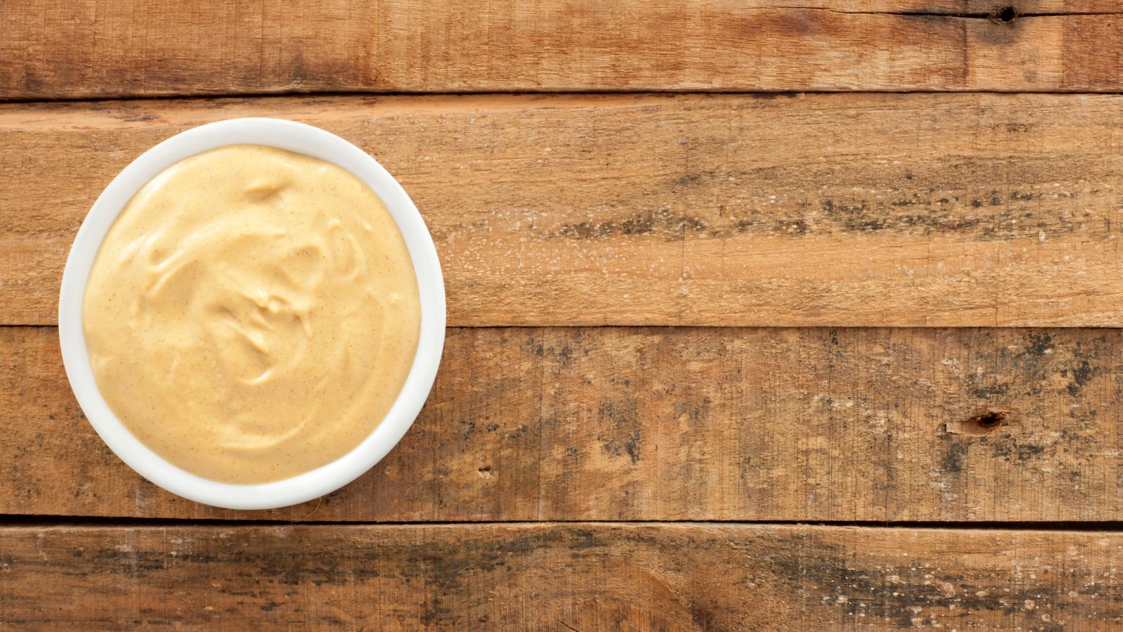 Creamy dijon mustard in a white bowl on wooden table.
