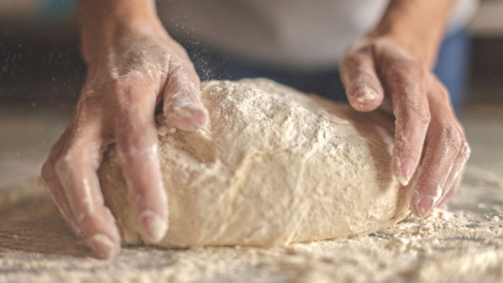 Hands kneading dough on floured surface with motion blur.