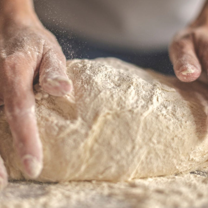 Hands kneading dough on floured surface with motion blur.