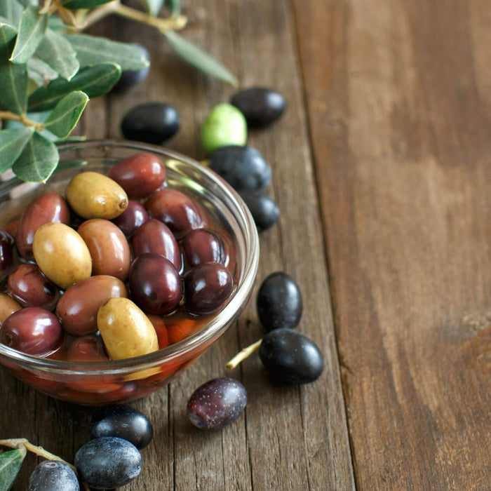 Bowl of mixed olives with olive branches on a rustic wooden surface.