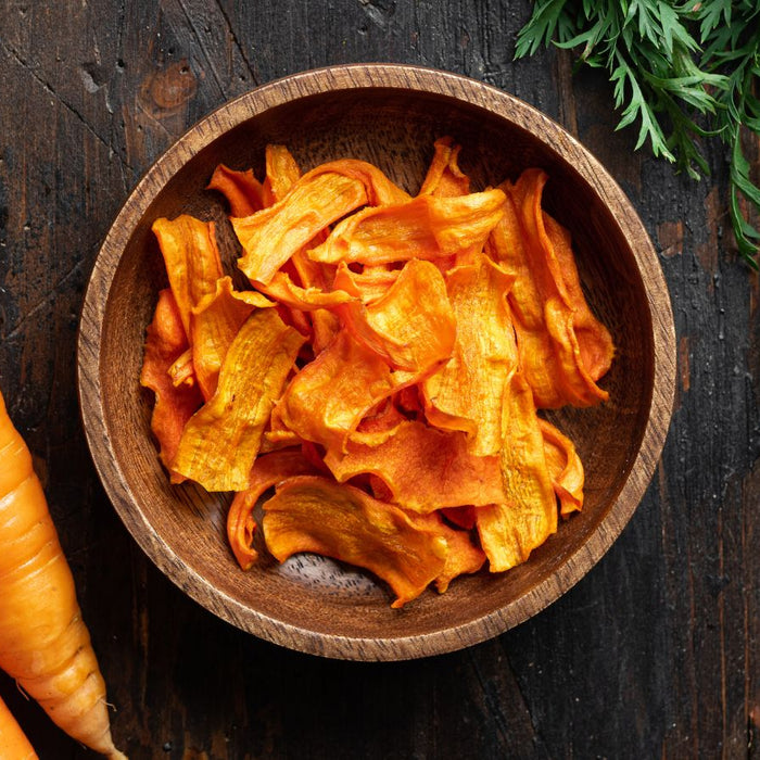 Wooden bowl filled with crispy carrot chips next to fresh carrots.
