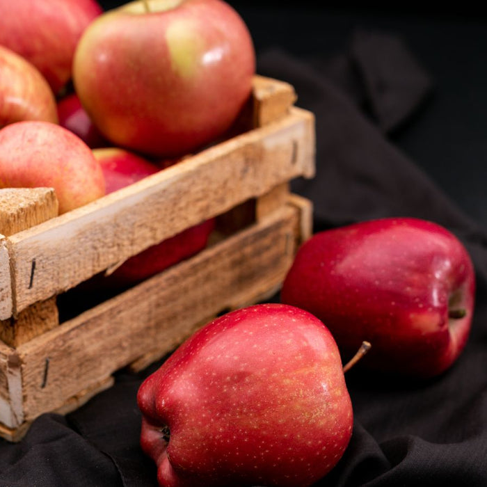 Fresh red apples in a rustic wooden crate on black cloth.