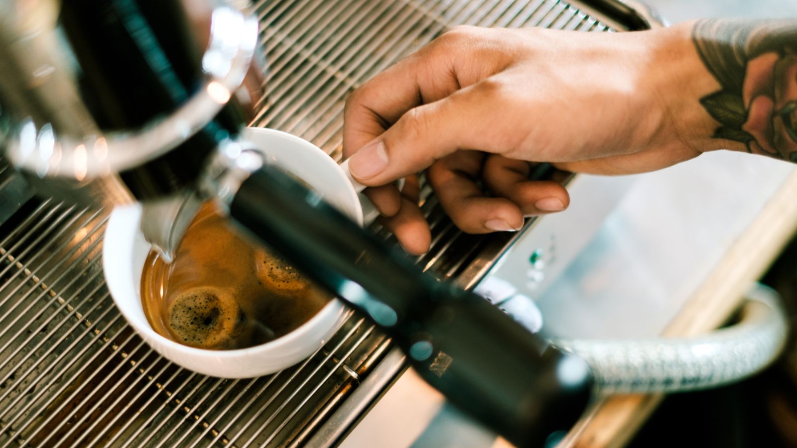 Espresso shot being pulled with a hand adjusting the cup