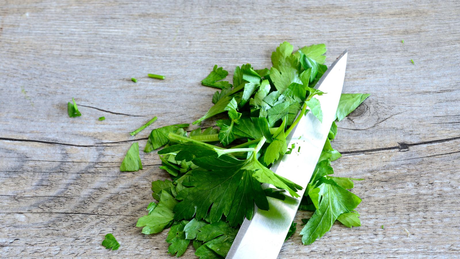 Chopped fresh parsley with knife on wooden cutting board.