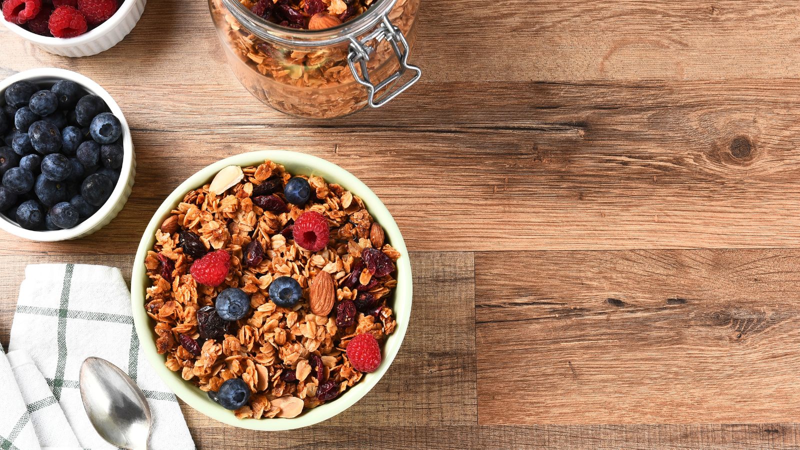 Granola cereal with berries and almonds in a bowl on wooden table.