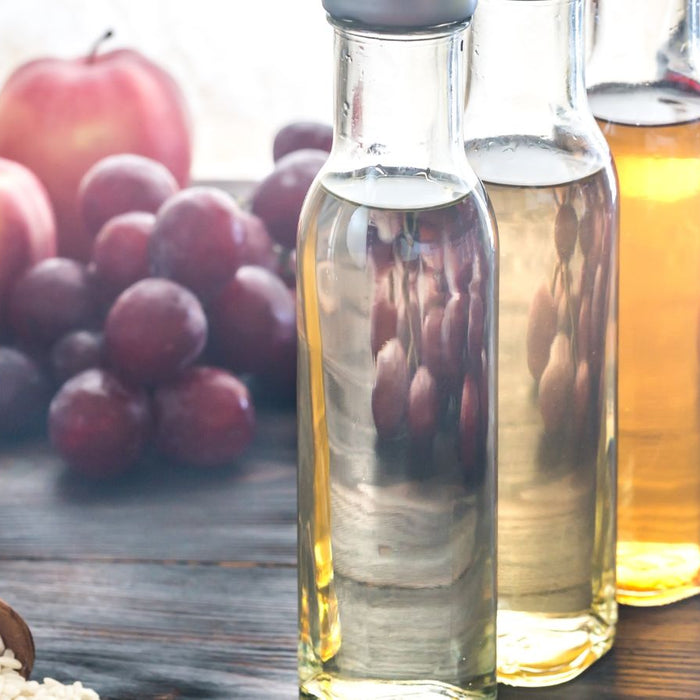 Assorted vinegar bottles with apples and grapes in background.