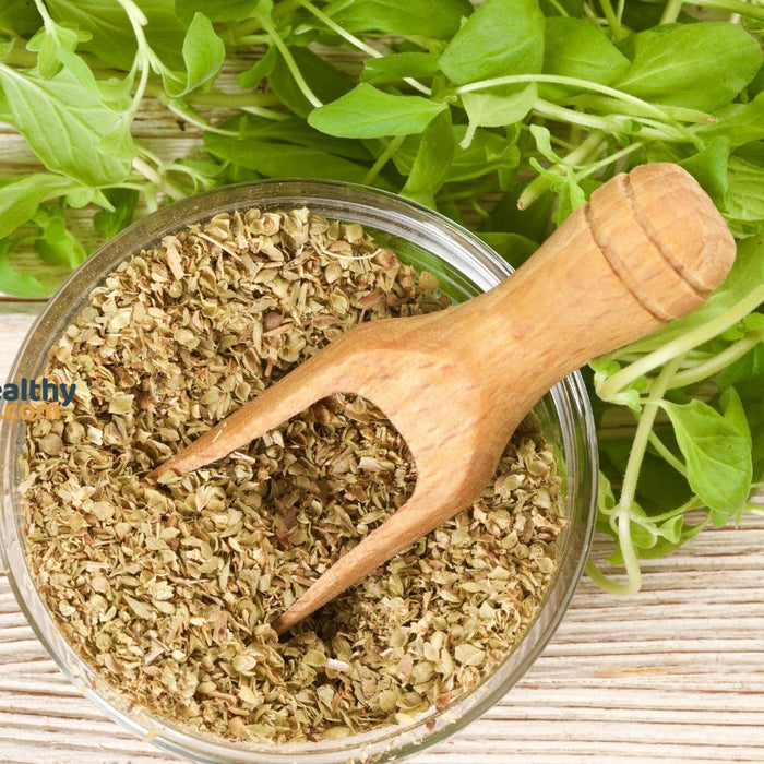 Dried oregano in bowl with fresh herbs on wooden background.