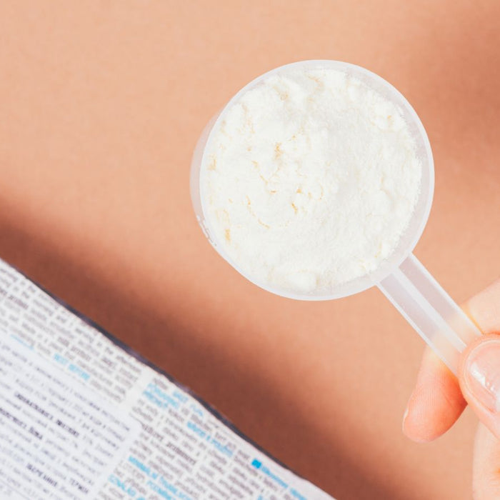 Hand holding scoop of white protein powder above product label