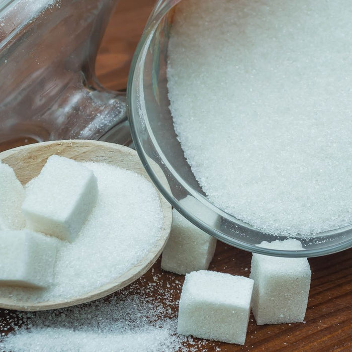 Jar of white sugar with cubes on wooden spoon and tabletop.