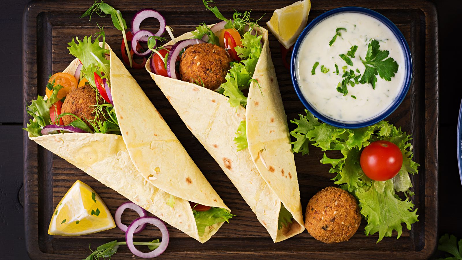 Tortilla wraps with fresh vegetables and yogurt sauce on wooden board